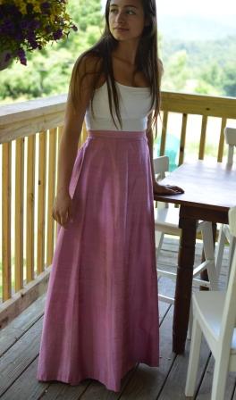 Young Brunette woman standing beside a able on a porch wearing a white spaghetti strapped top and 209 Walking skirt.