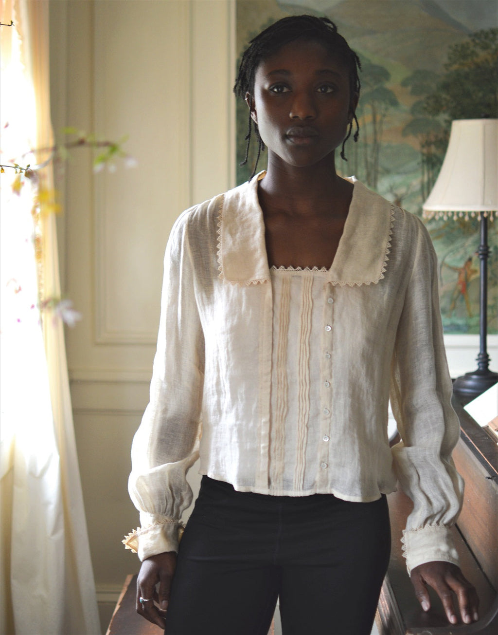 African woman standing in a room beside a piano wearing 210 Armistice Blouse and black leggings.