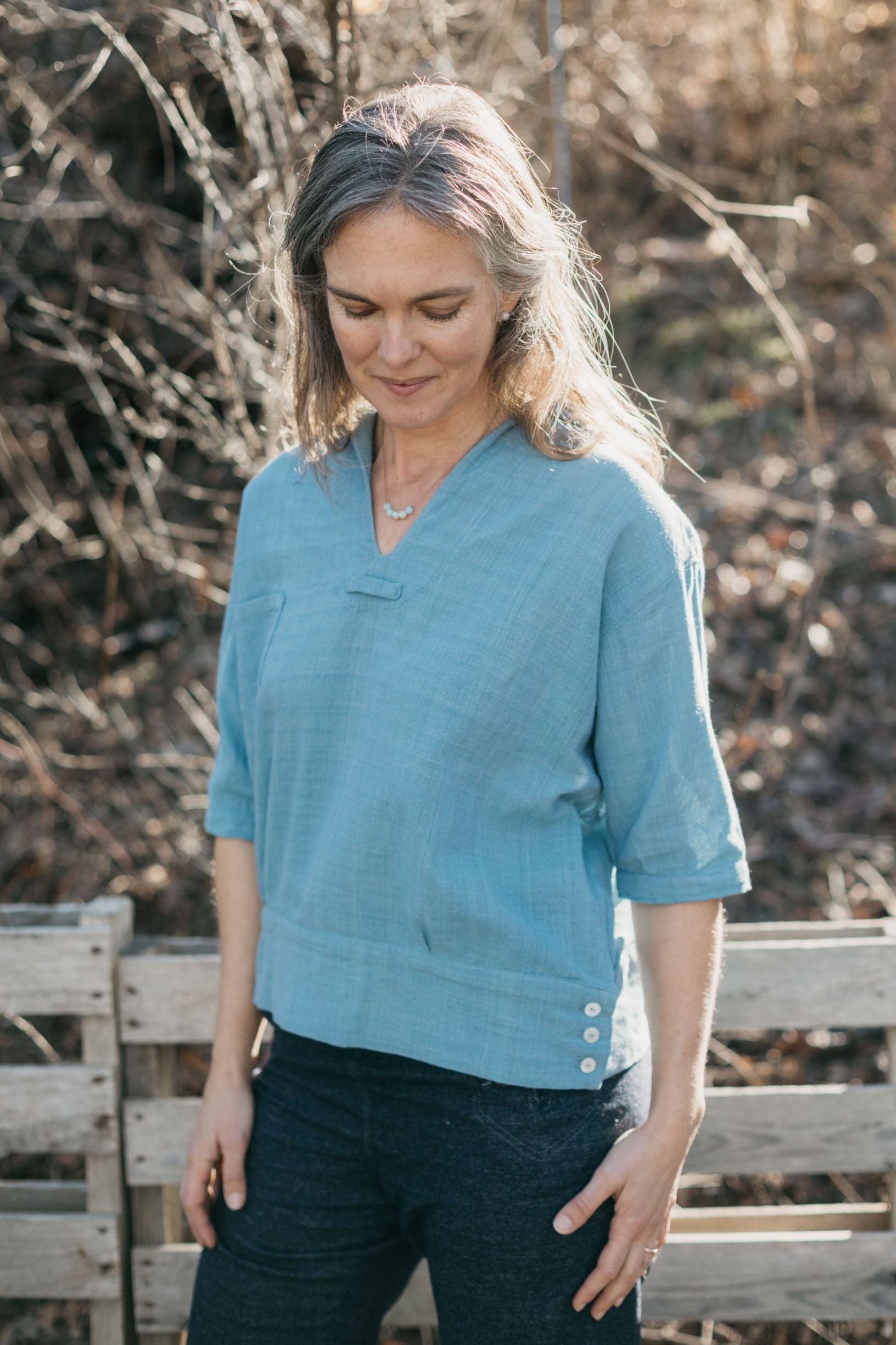 A white woman standing outside looking down wearing the 211 Two Middies v-neck