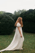 Side view of red head young woman standing surrounded greenery wearing 215 Empire Dress.