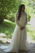 Young brunette woman standing on a wooden platform surrounded by greenery, wearing 227 Edwardian Bridal Gown and Dress.