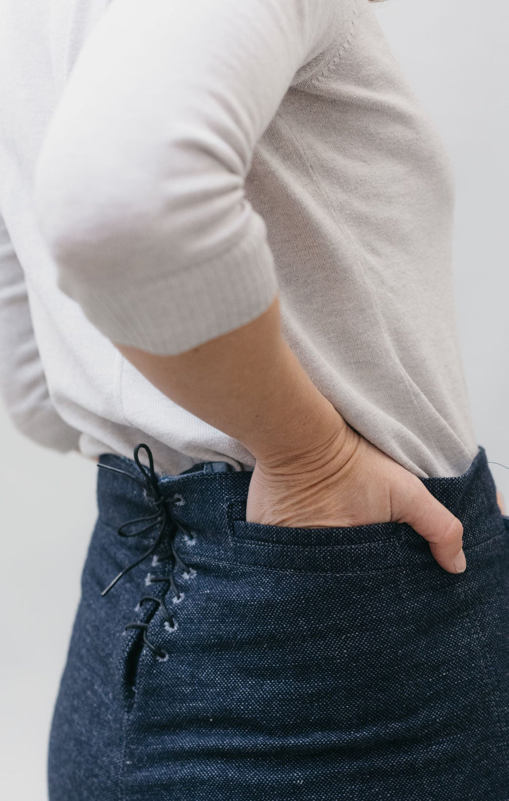 back side view of 229 Sailor Pants with hand in the welt pocket, and the laced up back.