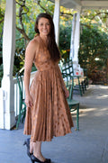 Woman wearing a brown polka dot blonde bombshell dress on a covered porch.