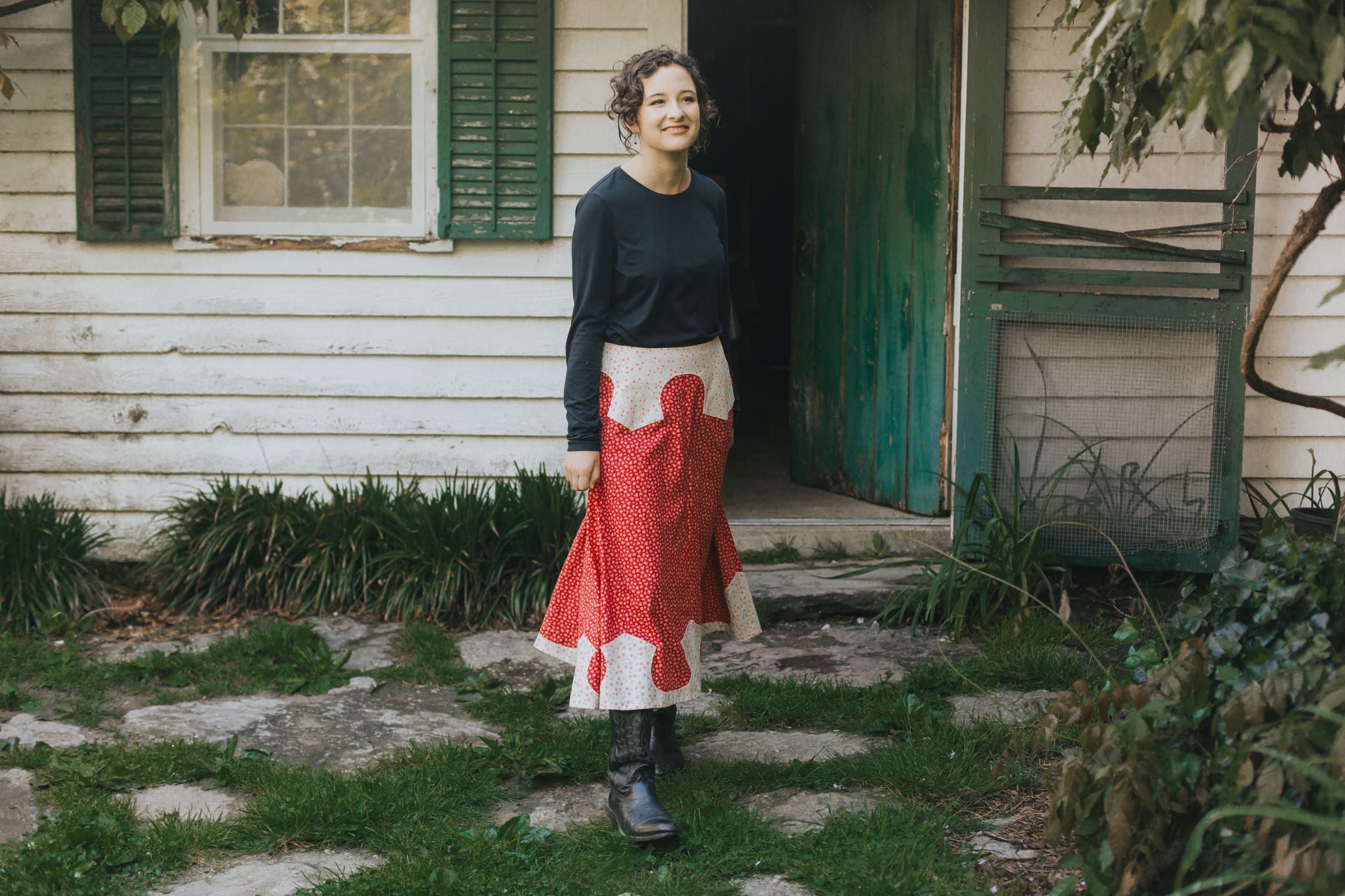 Young brunette white woman walking and smiling in front of a house surrounded by greenery wearing 243 Rodeo Cowgirl Skirt