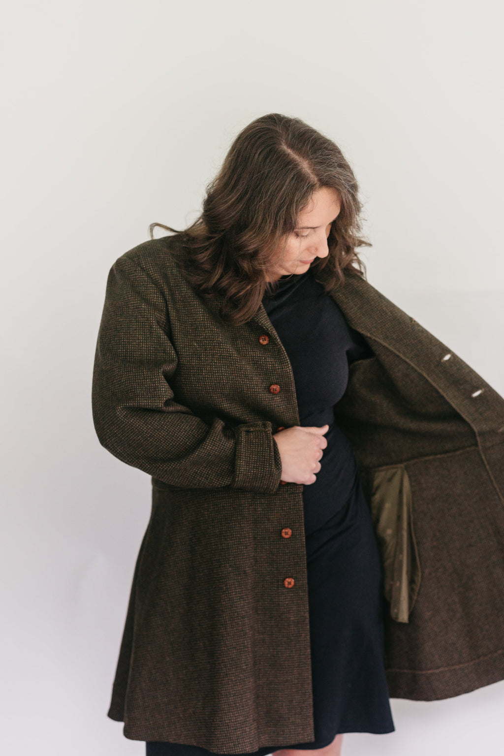 Brunette White woman wearing a black dress underneath the Countryside Frock Coat opening the left side of her jacket showing the inside.