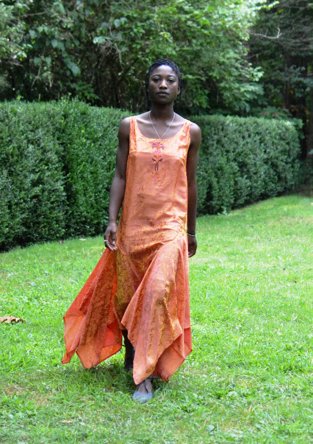 Young African woman standing surrounded by greenery wearing #264 Monte Carlo Dress in orange.