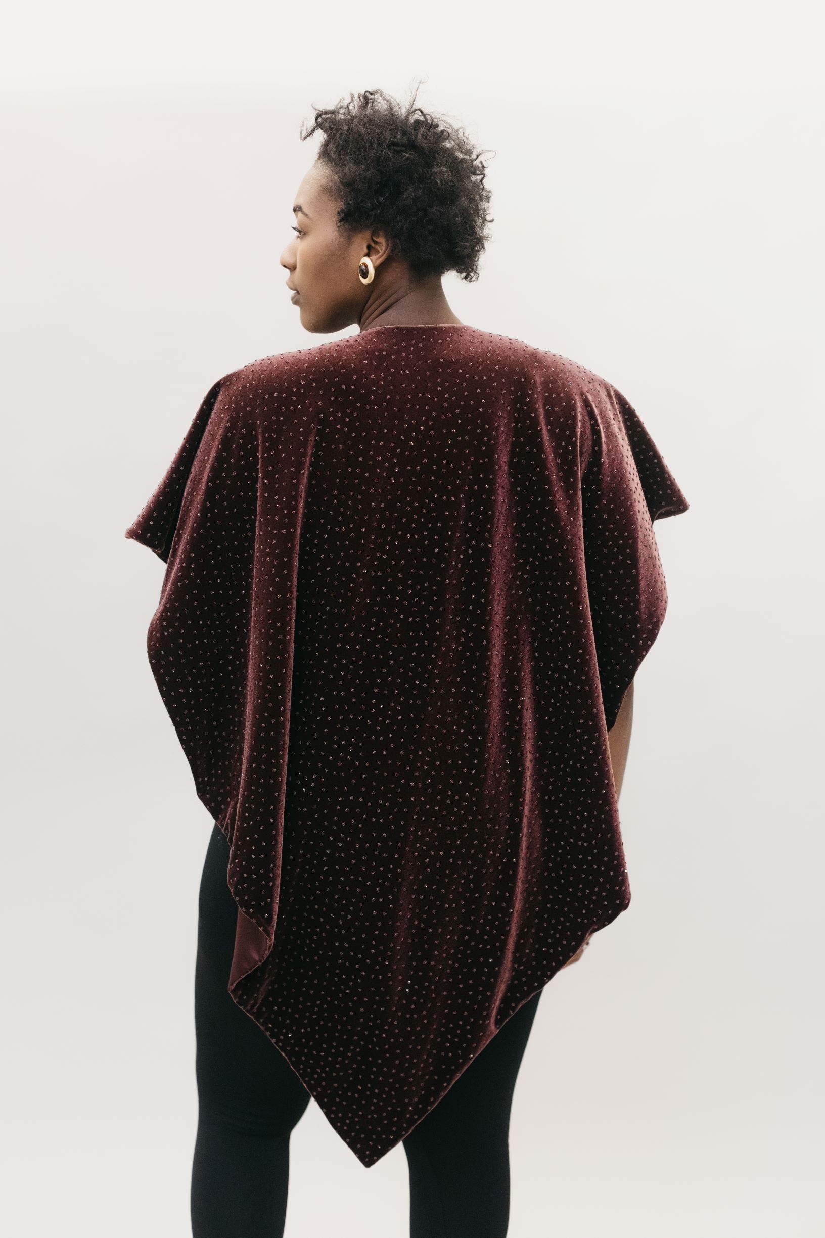 Back view of African American woman with short black hair wearing the Monte Carlo V-Neck Tunic in  maroon in front of a white studio backdrop head turned to the left.