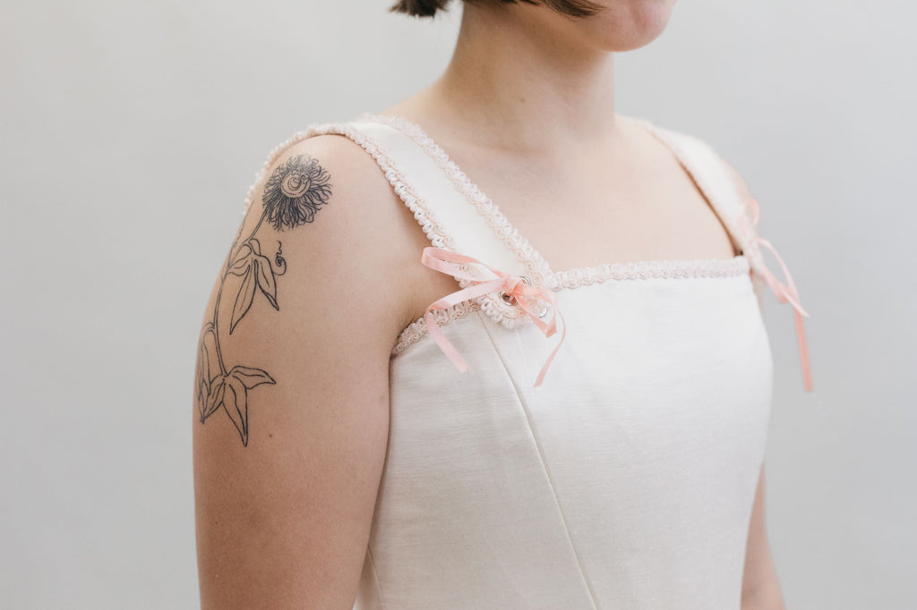 White woman wearing a square neck #267 M' Lady's Corset in white with pink bows on the base of the straps.